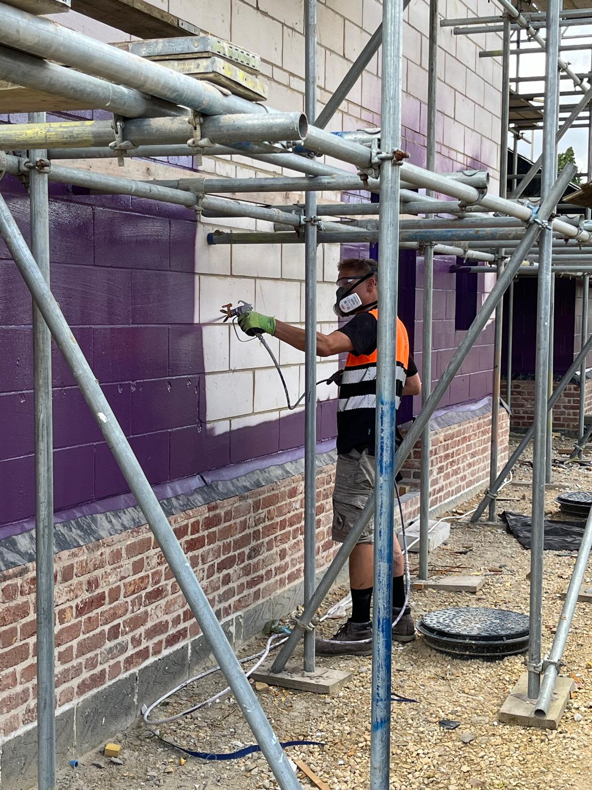 Worker applying Passive Purple External airtight and breathable membrane to exterior walls for weather protection and airtightness
